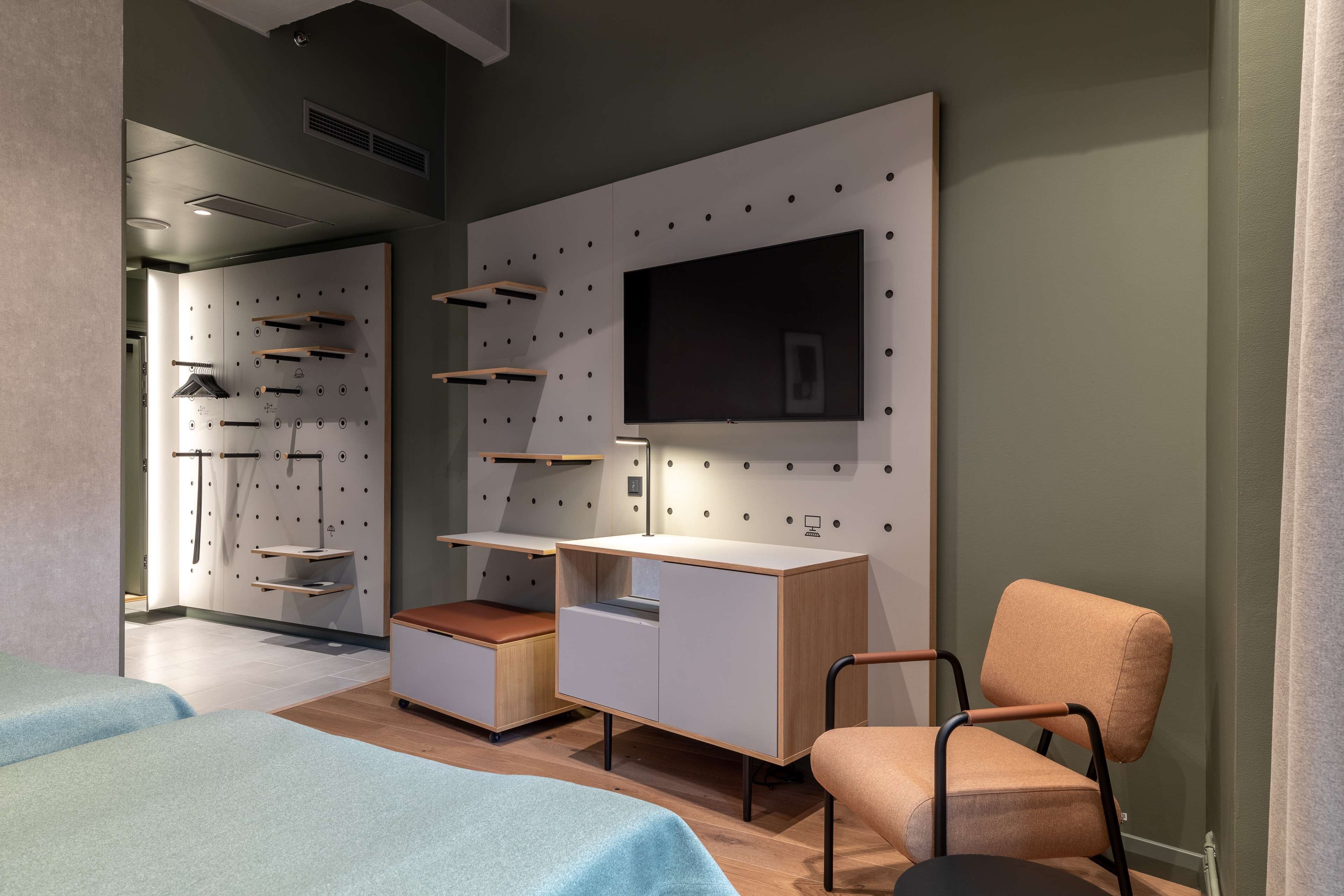 A modern room with a bed, a desk, a chair, and a TV mounted on the wall.