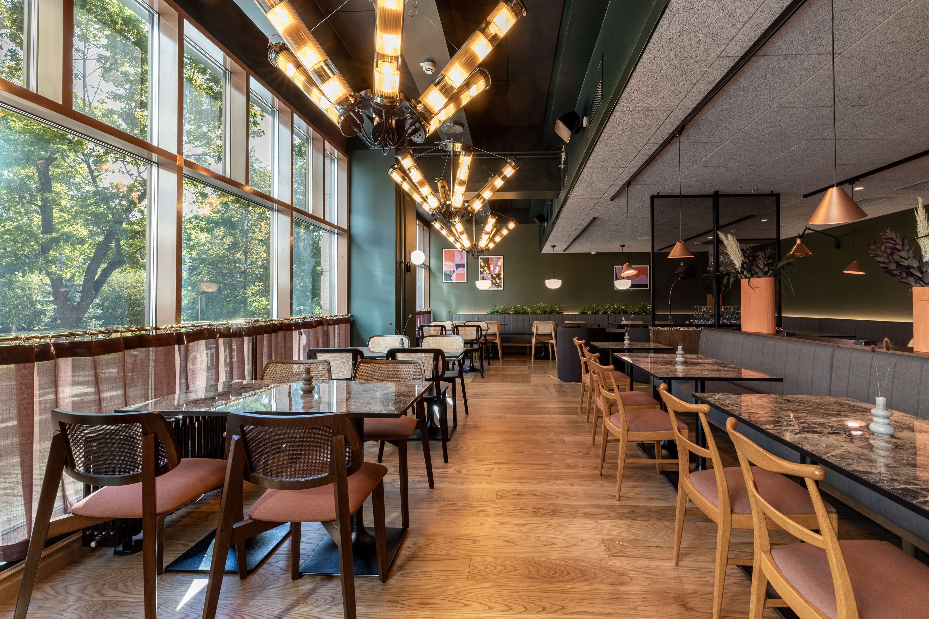 Ein Restaurant mit hohen Decken, großen Fenstern und verschiedenen Sitzmöglichkeiten, darunter Tische und Sitzbänke.