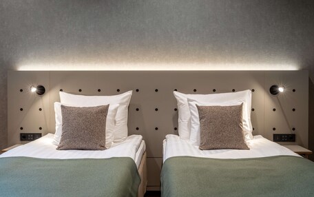A double room with two beds, each with a pillow and a green blanket.