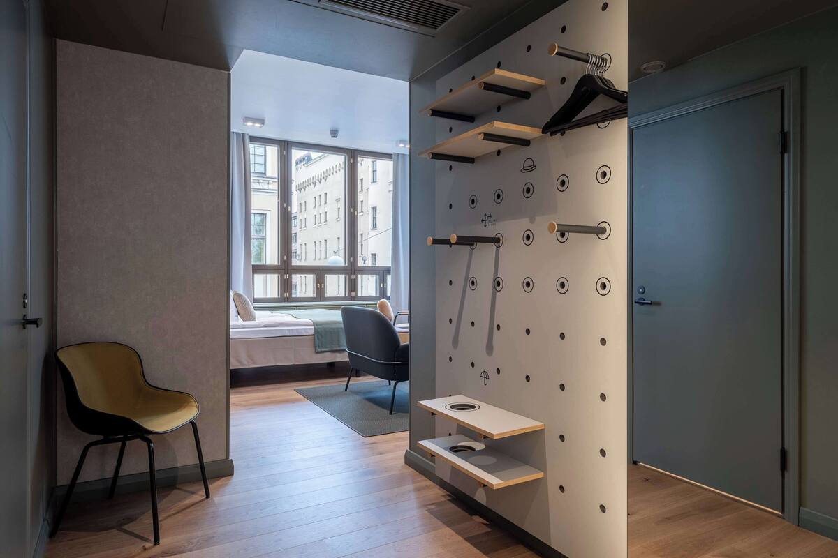 Une chambre moderne avec un plancher en bois, une chaise jaune, un lit avec vue et un porte-manteau mural avec des crochets.