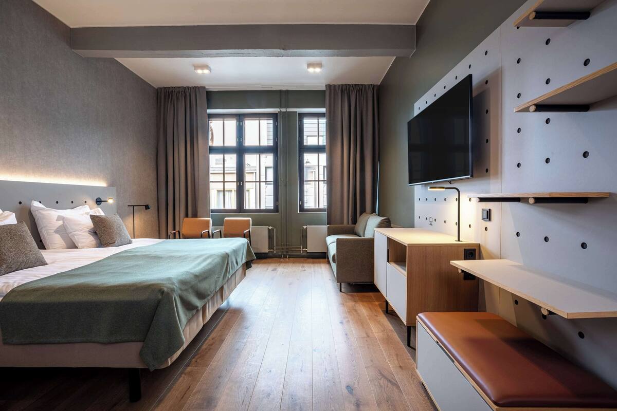 Une chambre d’hôtel moderne équipée d’un grand lit, d’un bureau, d’une télévision et d’une fenêtre avec des rideaux.