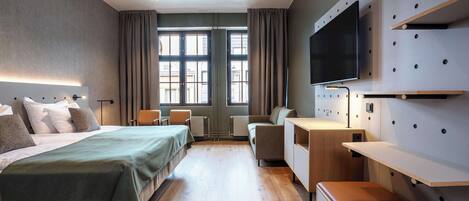 Et moderne hotelværelse med en stor seng, et skrivebord, et fjernsyn og et vindue med gardiner.