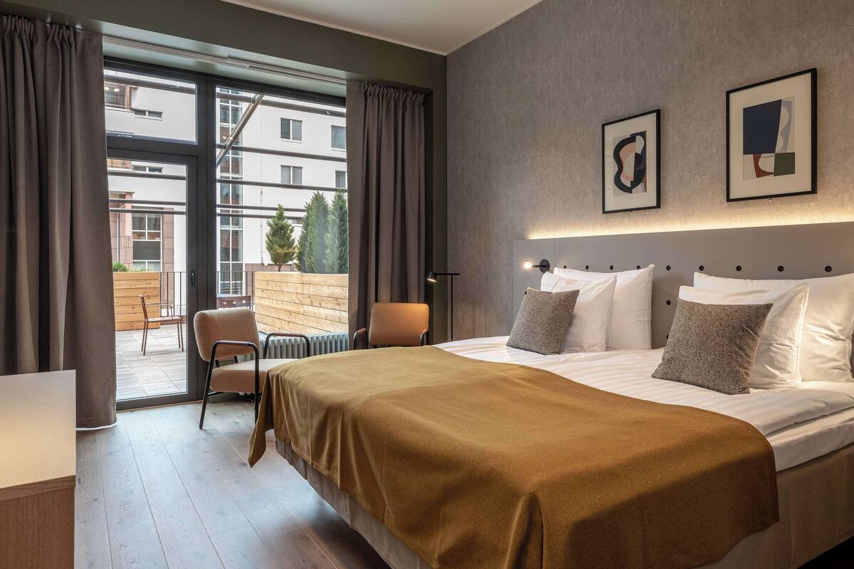 Une chambre d’hôtel moderne, dotée d’un grand lit, d’une chaise, d’une table et offrant une vue sur l’extérieur.