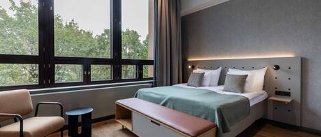 A modern bedroom with a large window, a bed with a headboard, a bench, and a small table.