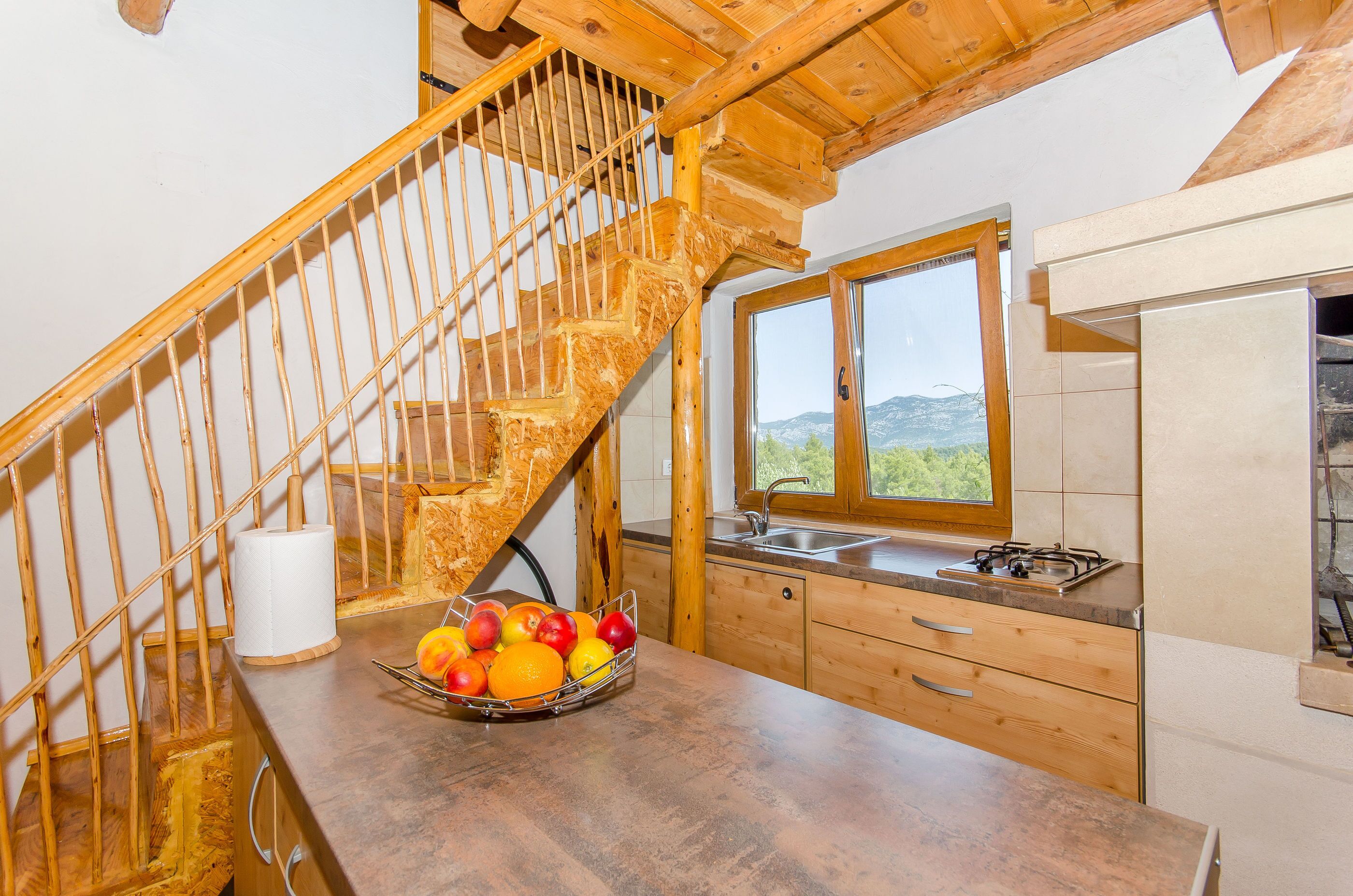 Una cocina con una escalera de madera, una ventana con vistas y una cesta de frutas sobre la encimera.