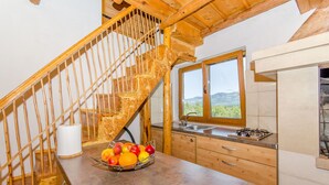 Une cuisine avec un escalier en bois, une fenêtre donnant sur un beau paysage et un panier de fruits posé sur le comptoir.