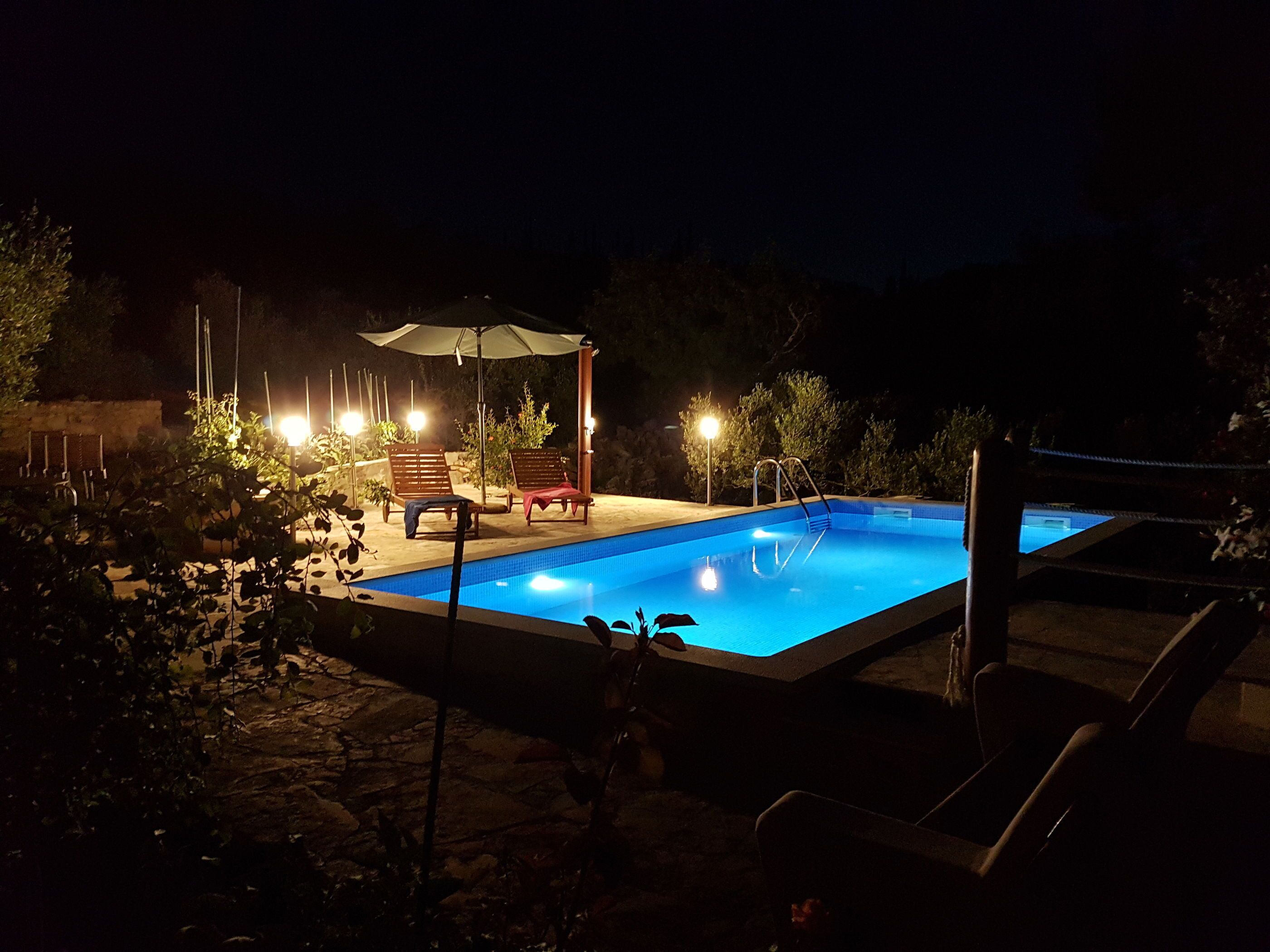 A swimming pool with lounge chairs and umbrellas, surrounded by trees and a stone wall.