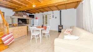 Un salon chaleureux avec un plafond en bois, un canapé, une table à manger avec des chaises et un coin cuisine équipé d’une cuisinière et de placards.