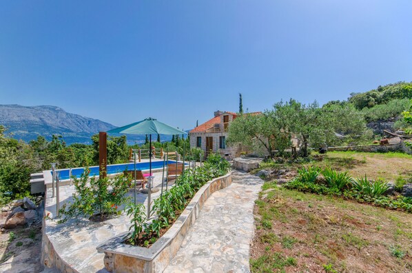 A pool area with a stone pathway, a blue umbrella, and a view of mountains.