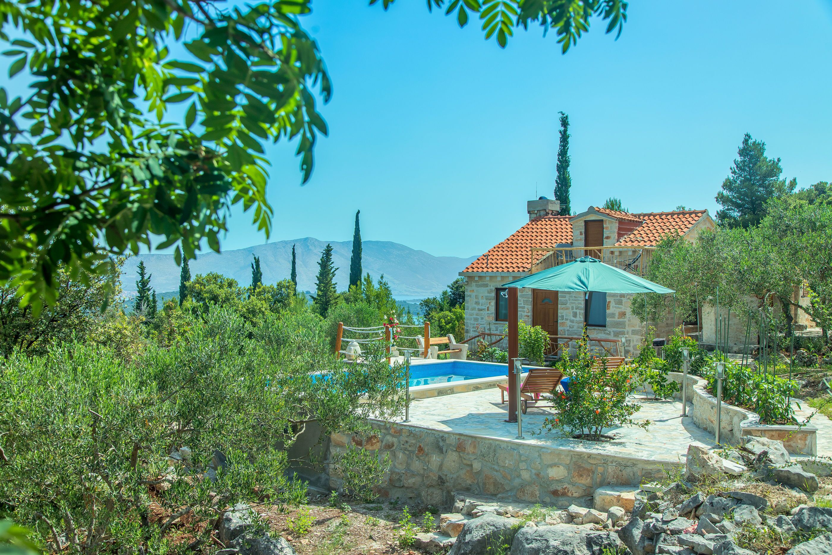 Una casa de piedra con piscina, rodeada de vegetación y montañas al fondo.