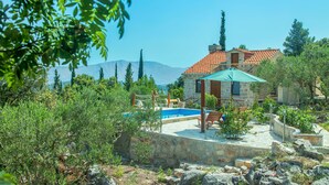 Une maison en pierre avec une piscine, entourée de verdure et avec des montagnes en toile de fond.