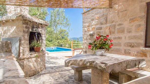 Une terrasse en pierre avec une piscine, des murs en pierre et une table agrémentée d’une plante en pot.