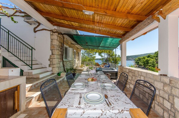 Un espace de restauration extérieur abrité, doté de murs en pierre, d’un plafond en bois et offrant une vue sur la mer.