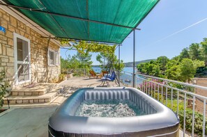 Un espace extérieur avec un jacuzzi, un bâtiment en pierre, une terrasse couverte avec des chaises et une vue sur la mer.