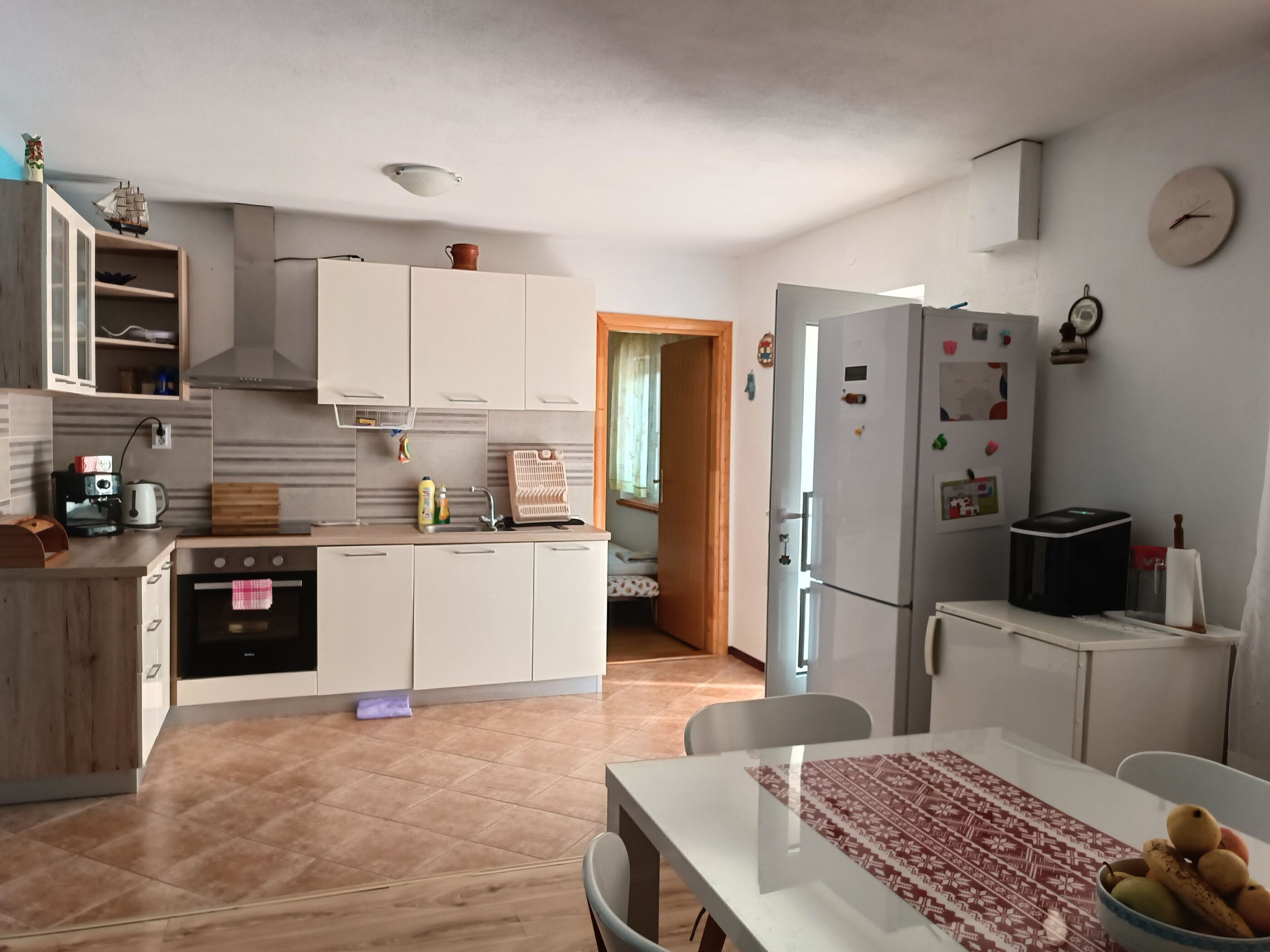 A modern kitchen with white cabinets, a built-in oven, a coffee machine, and a refrigerator.