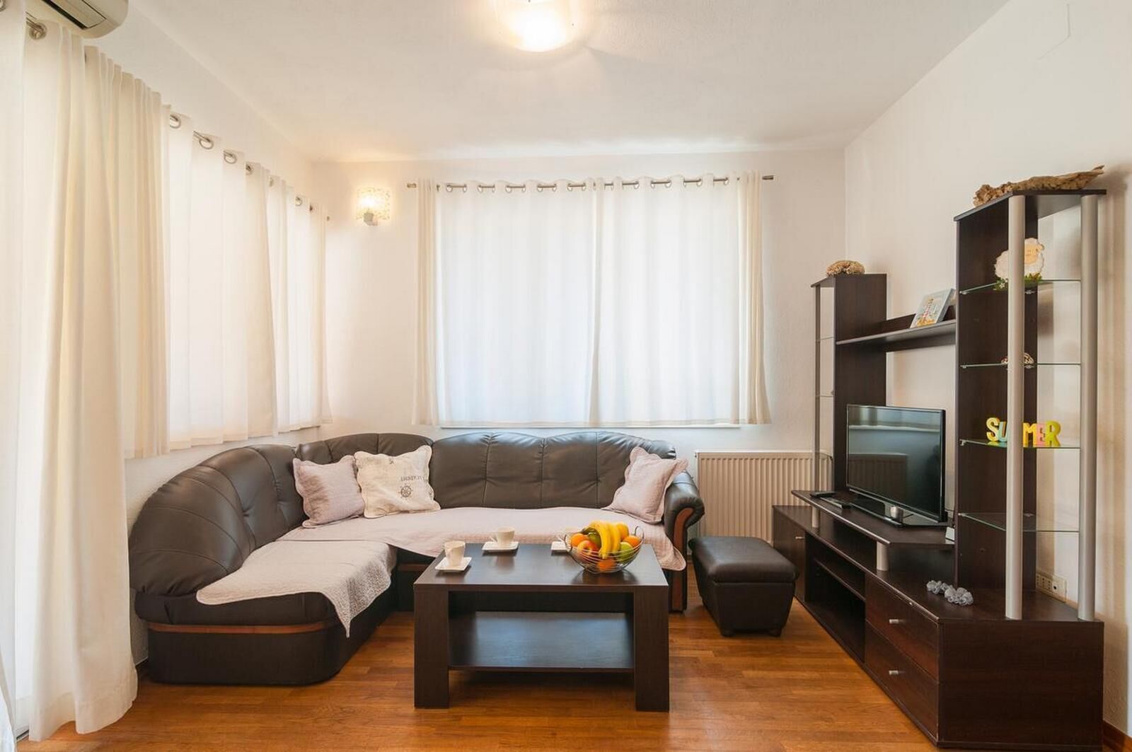 A living room with a dark leather sofa, a coffee table with fruits, a TV, and a bookshelf.