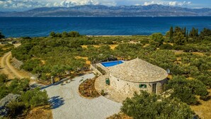 Une maison en pierre à plan circulaire, dotée d’une piscine et offrant une vue sur la mer et les montagnes.