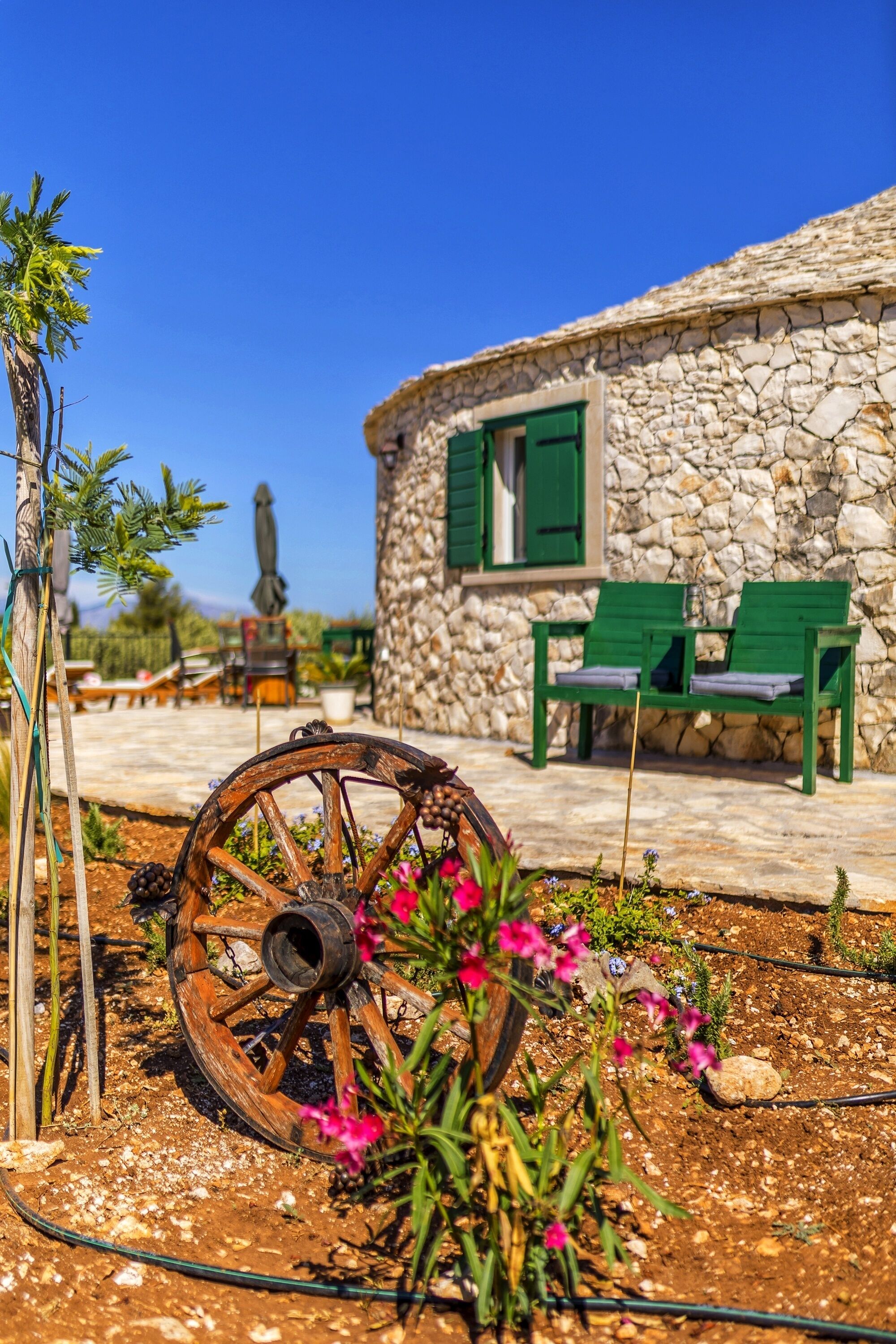 A stone building with green shutters, a wooden cart, and outdoor seating.