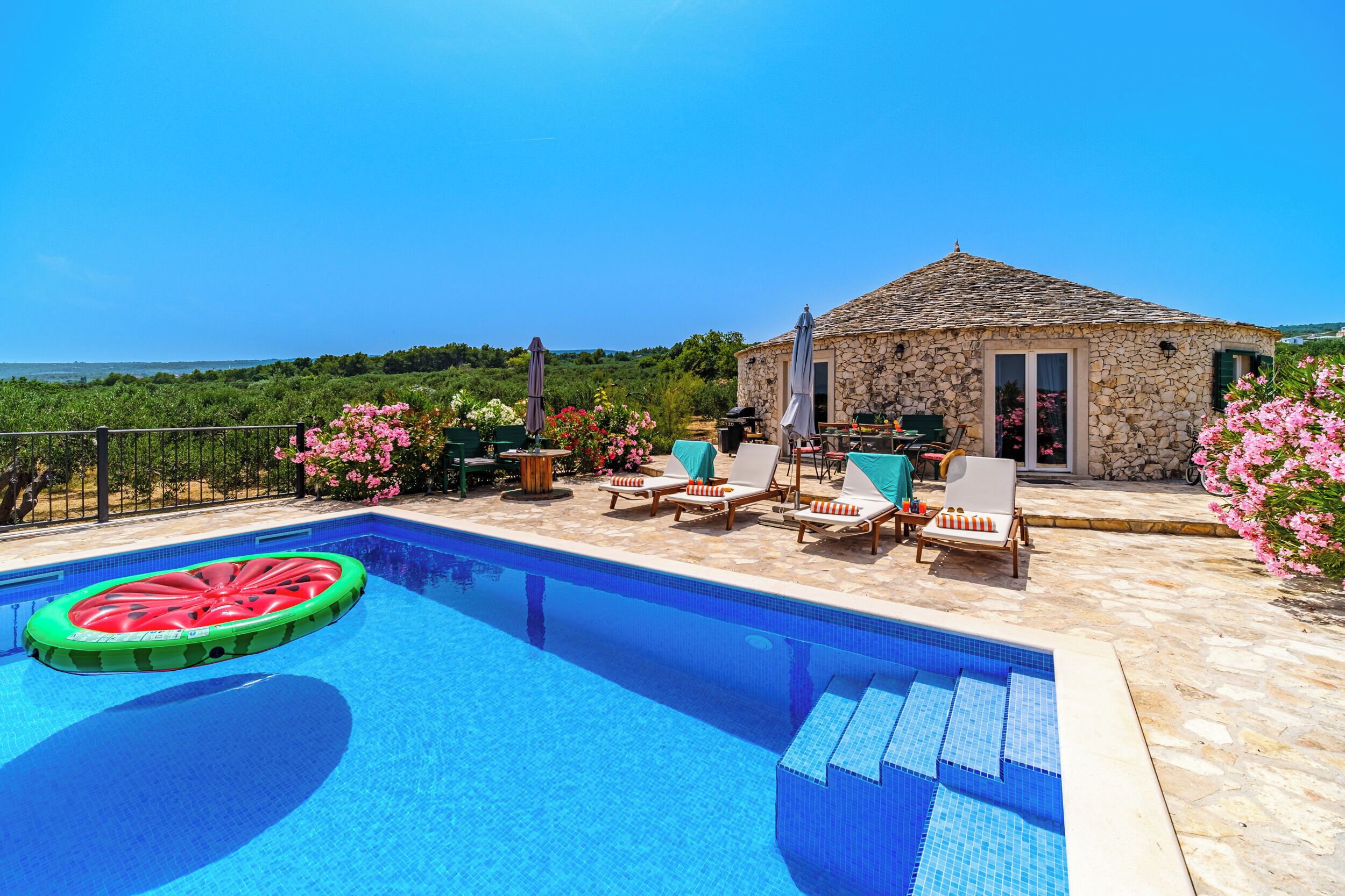 A pool with lounge chairs and a stone building with a tiled roof.