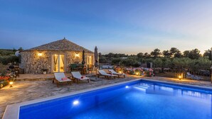 Un bâtiment en pierre avec un toit en tuiles, une piscine et des chaises longues.
