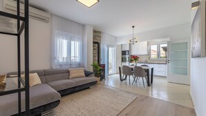 Un salon moderne avec un canapé gris, une table à manger avec des chaises, et une cuisine en arrière-plan.
