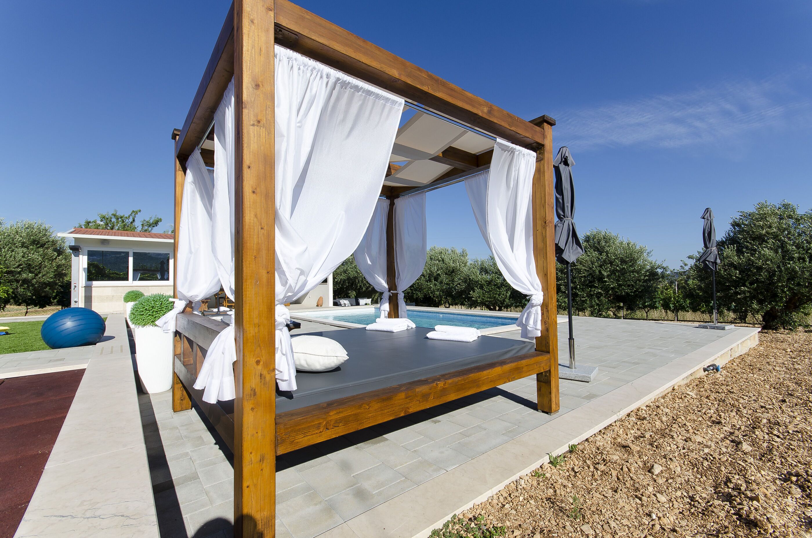 A wooden canopy bed with white curtains, a pool, and a well-maintained garden.