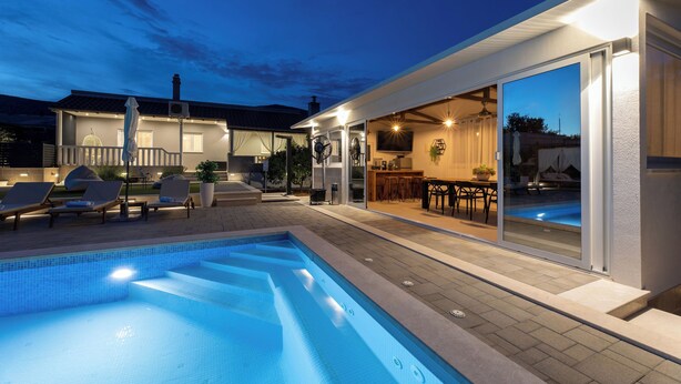 Une maison moderne dotée d’une piscine, d’un espace salon extérieur et d’un bar.