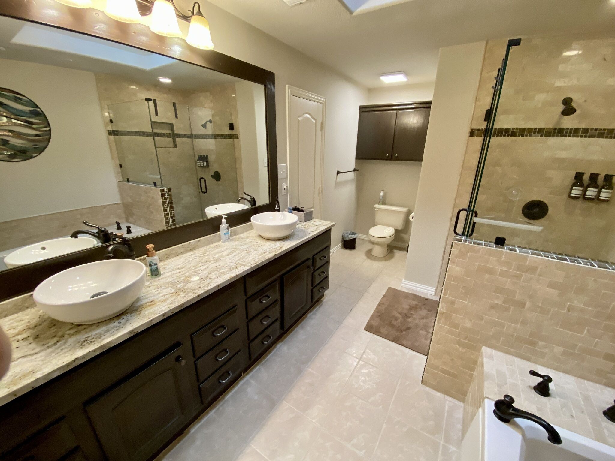 A modern bathroom with two sinks, a large mirror, a shower area, and a toilet.