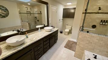A modern bathroom with two sinks, a large mirror, a shower area, and a toilet.
