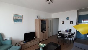 A modern living room with a sofa, a coffee table, a TV, and a dining area with chairs and a table. - SEAFRONT APARTMENT 60 M2 AND LOGGIA (Saint-Jean-de-Monts)