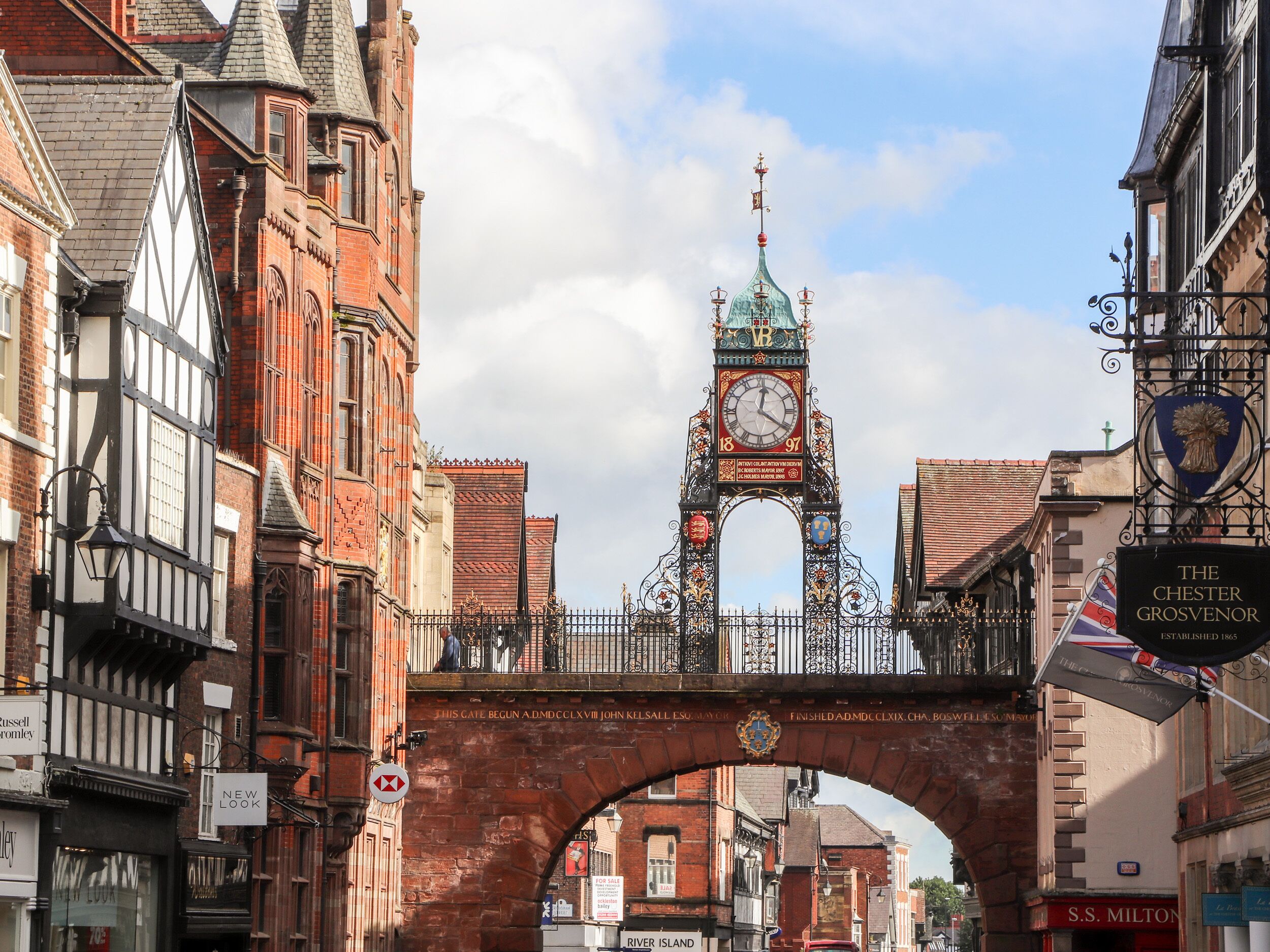 Un puente histórico con una torre del reloj, rodeado de arquitectura tradicional y comercios.