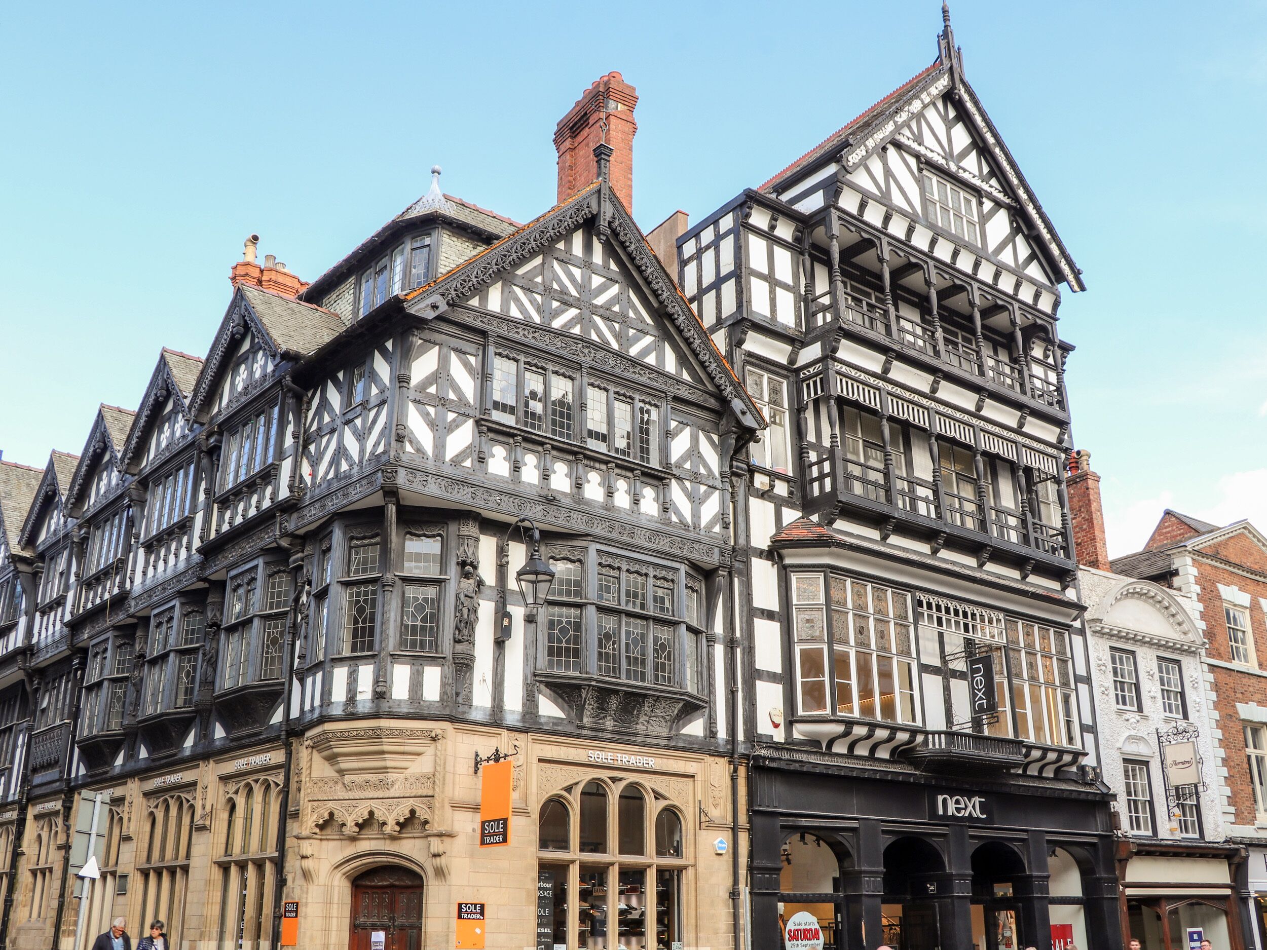 A historic building with Tudor-style architecture, featuring a prominent corner with a black and white timber frame, large windows, and a sign for Sole Trader.