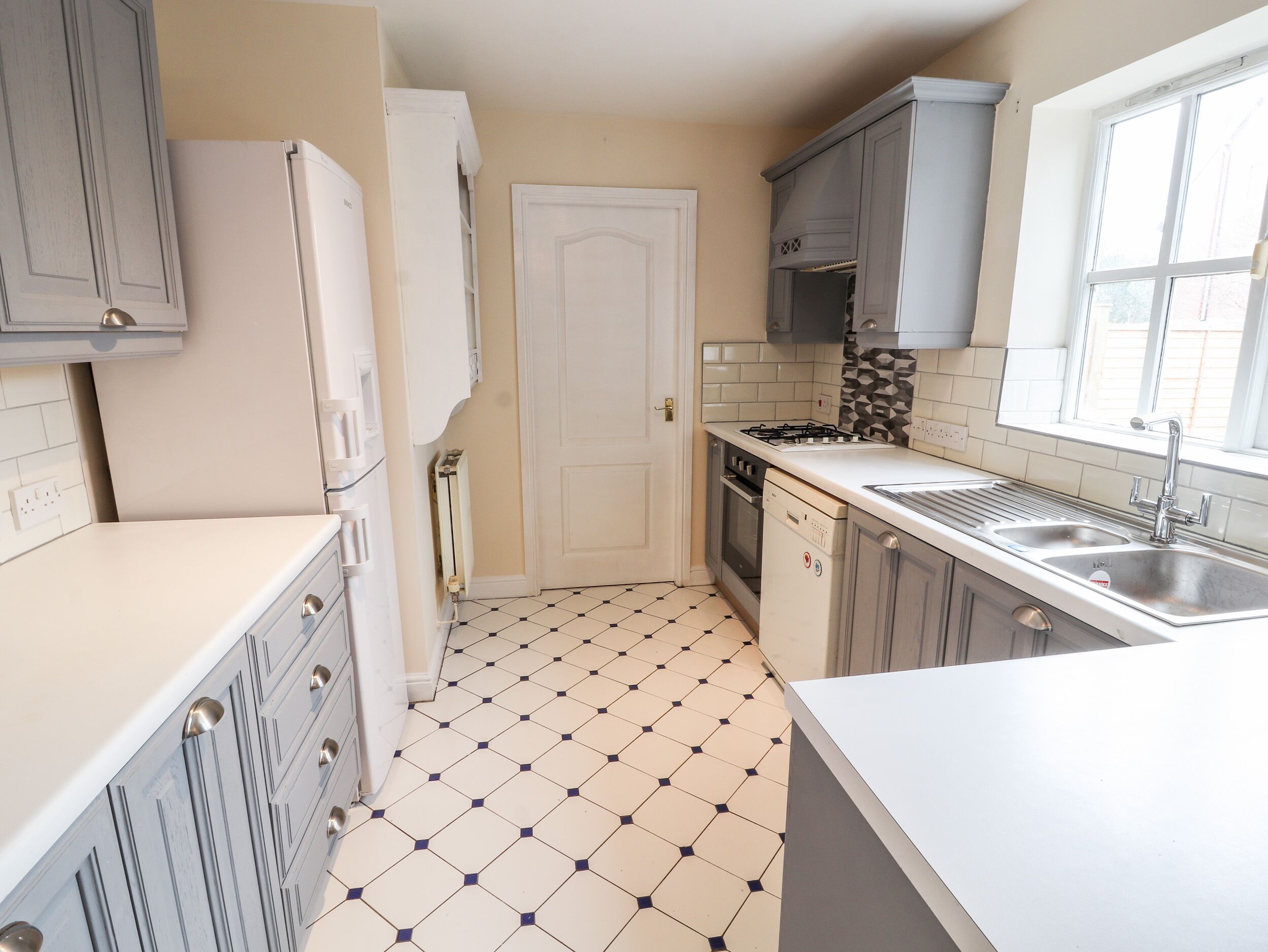 A kitchen with white cabinets, a tiled floor, a stove, a sink, and a window.