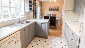 A compact kitchen with grey cabinets, a Bosch dishwasher, a tiled floor, and a dining area with a table and chairs. - 45 Benton (Chester)