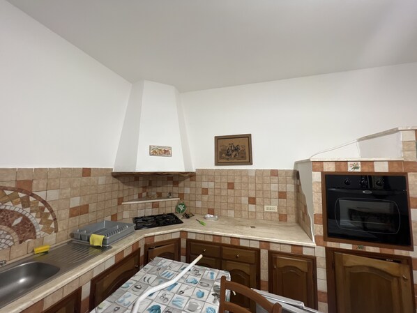 A compact kitchen with a gas stove, oven, and a sink. There are cabinets and a tiled backsplash. - Villa Maccioni No. 3, Ocean View (Tanaunella)