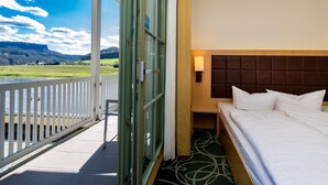 Quarto de hotel com uma cama, vista para uma paisagem verde e uma varanda com guarda-corpo.