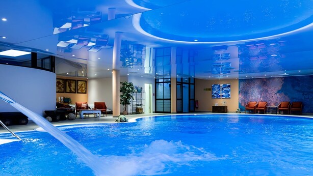 Uma piscina interior com design moderno, apresentando teto curvo e áreas de estar ao redor.
