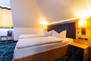 Habitación de hotel con una cama grande, dos mesitas de noche, una silla y un cabecero con iluminación integrada.