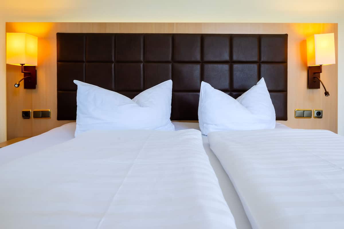 A hotel room with two beds, a dark headboard, and wall-mounted lamps.