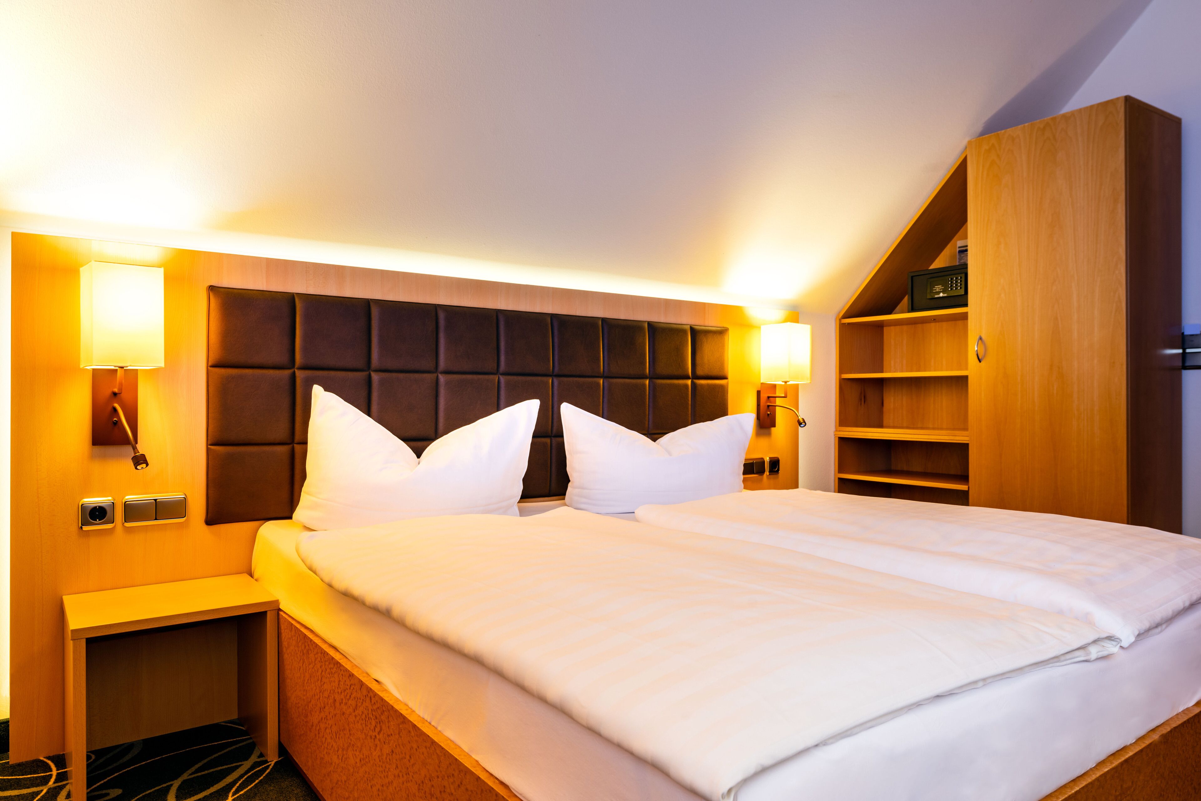 Habitación de hotel con una cama grande, dos lámparas de noche, un armario de madera y estantería empotrada.