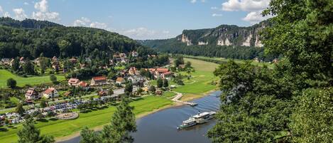 A riverside town with houses, a boat, and a forested hill.