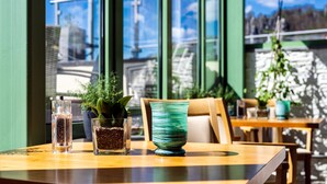 Mesa de restaurante com um copo, uma planta em vaso e um vaso decorativo.