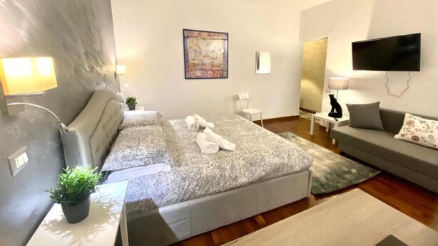 Moderni hotellihuone, jossa on suuri sänky, sohva, televisio ja taulu seinällä.