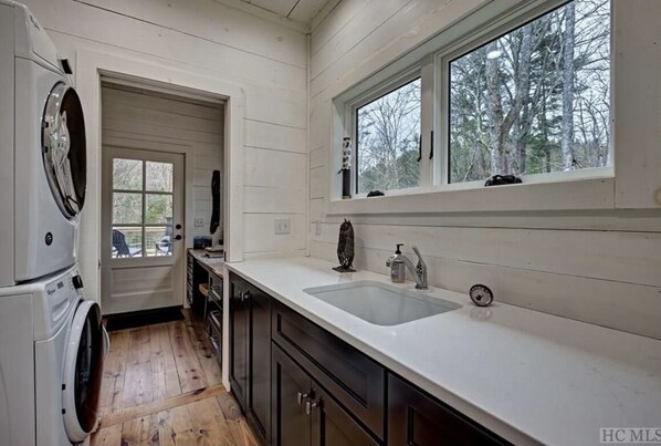 Una cocina compacta con lavadora, un lavabo y ventana con vistas a árboles.