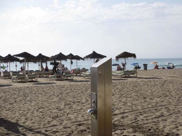 A beach with umbrellas, lounge chairs, and a metal structure in the foreground.