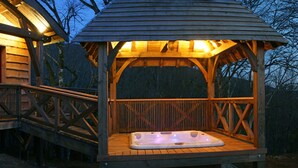 Une structure en bois abritant un bain à remous, dotée d’un toit et entourée d’une terrasse et d’une balustrade en bois.
