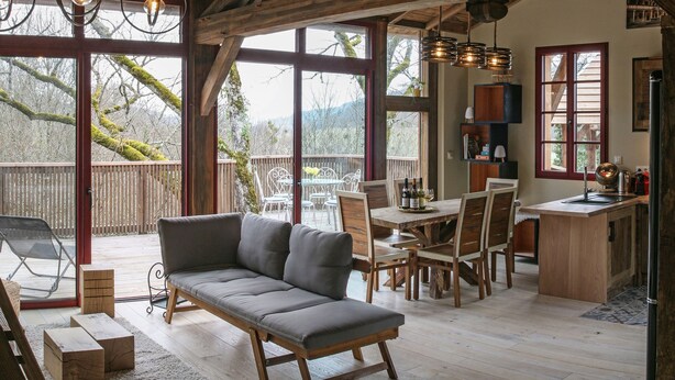 Un intérieur chaleureux avec un plafond en bois, un canapé, une table à manger, des chaises et un coin cuisine.