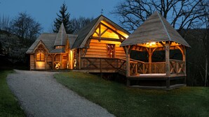 Une cabane en bois, accessible par un chemin de gravier, dotée d’un porche couvert et d’une cheminée.