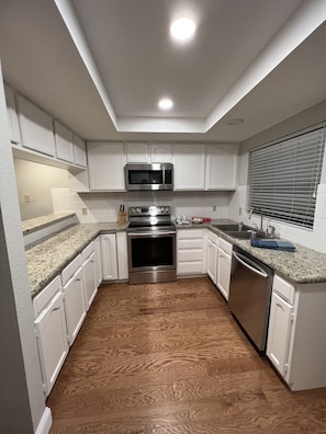 A kitchen with white cabinets, a stainless steel microwave, oven, and dishwasher, a granite countertop, and a wooden floor. - Spacious 2BD 2BA FreeWiFi Parking 12 mi - AT&T Stadium, Globe Life Field, TLive! (Arlington)