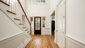 A hallway with wooden flooring, white walls, a wooden staircase, and a door with glass panels. - Pristine 2nd row home in Sea Pines w/ great outdoor space, private pool & spa (Hilton Head Island)
